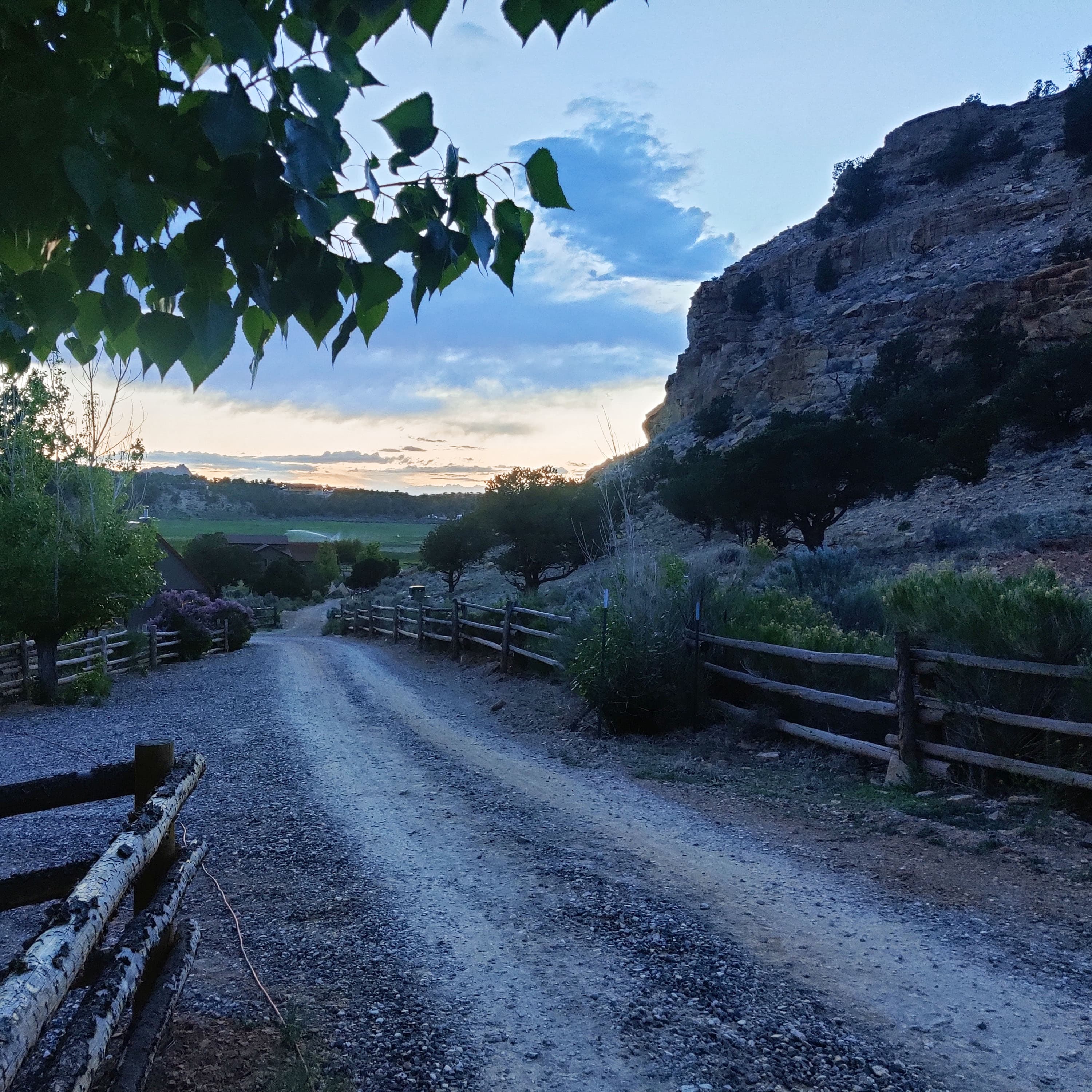the sunset, viewed along a dirt road with a fence on either side