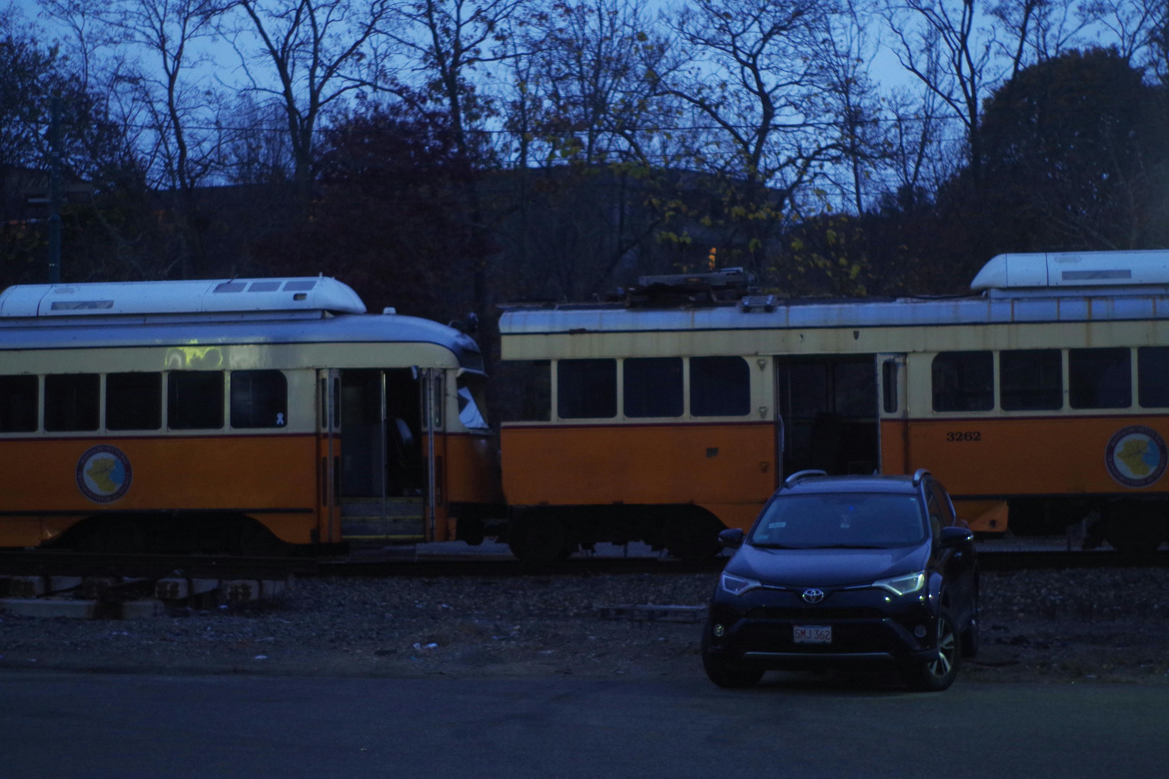 a picture of two streetcars in the train yard, one missing part of the car, with an SUV parked in front of them