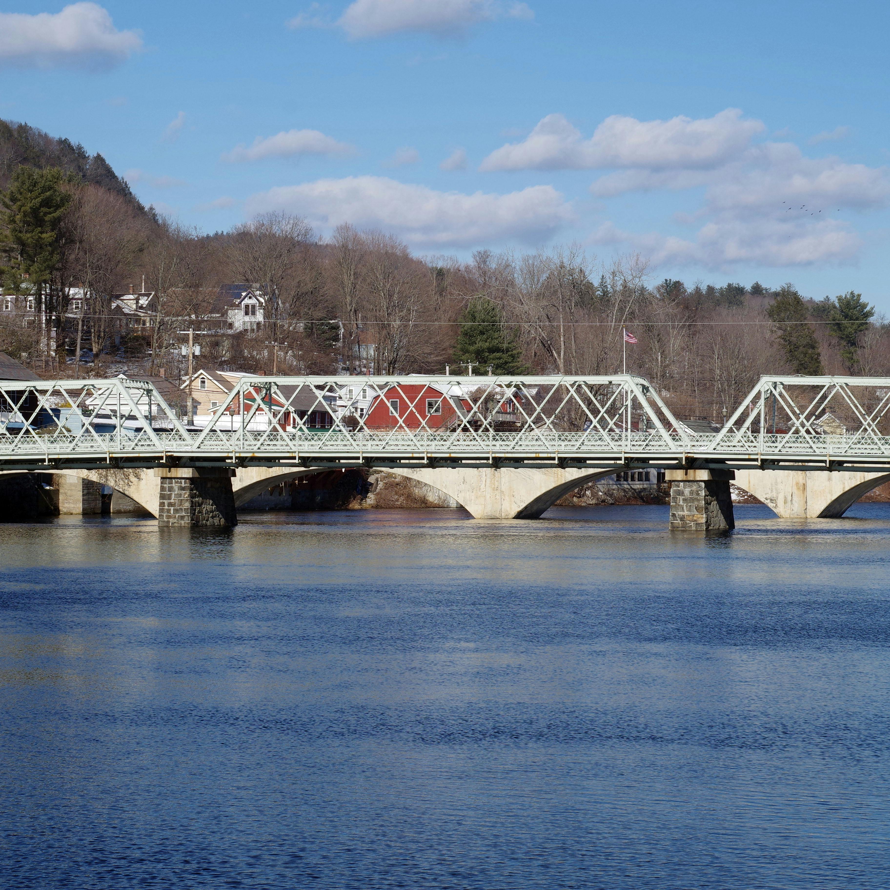 looking over a river at a truss bridge in the foreground and an arch bridge in the background